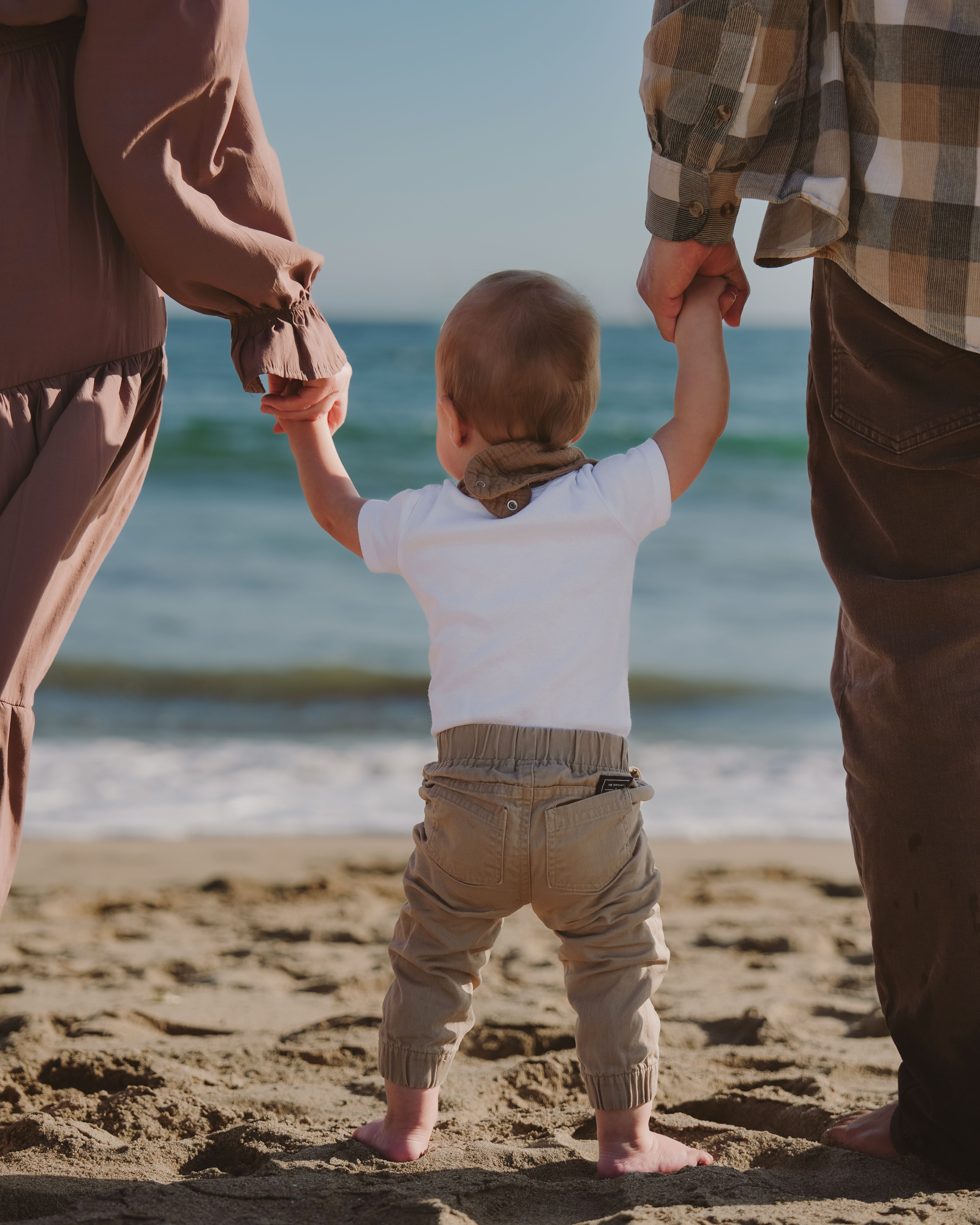 Baby walking with parents on a beach in Pacifica, California